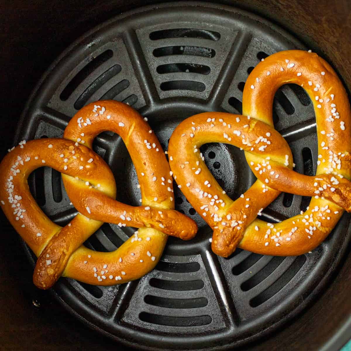 Two soft pretzels in an air fryer basket.